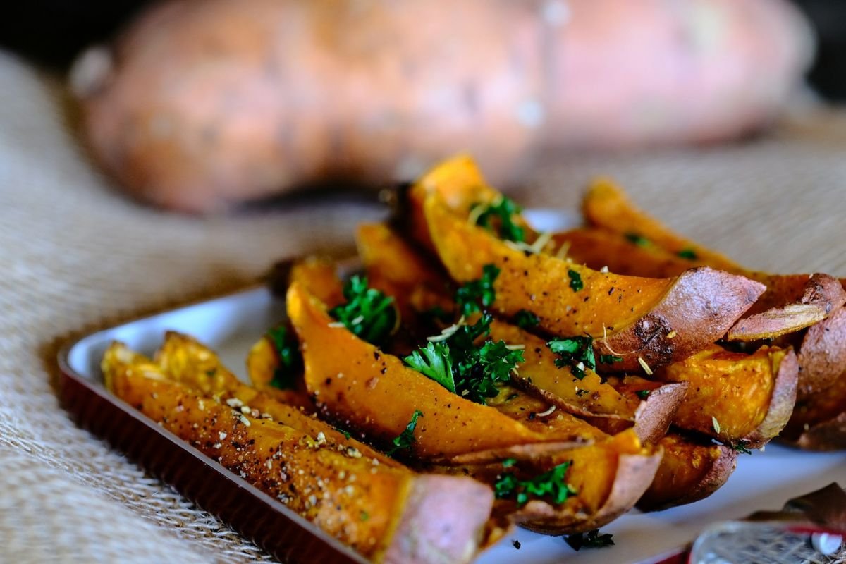 Crispy, Caramelised & Irresistible: The Best Way to Enjoy Sweet Potatoes Golden-brown roasted sweet potato slices on a rustic wooden chopping board, showcasing their caramelised edges and rich texture.