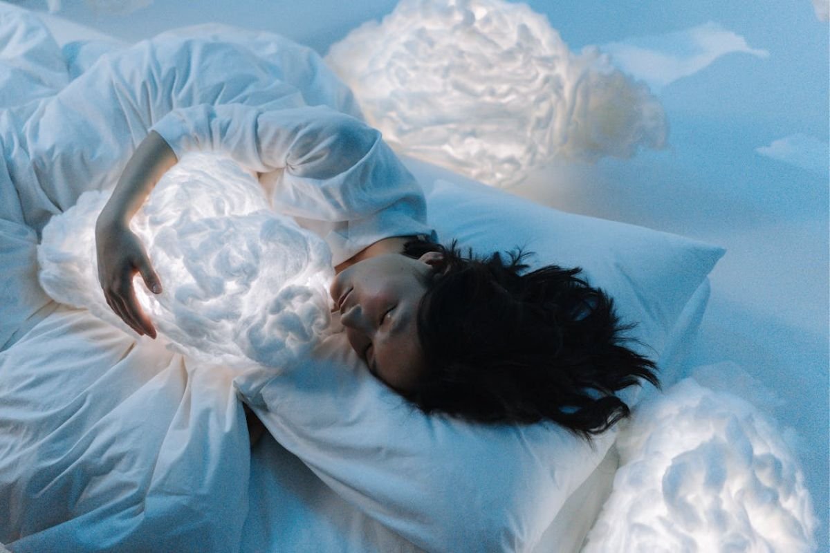 Woman peacefully sleeping while hugging a soft cloud, symbolising dream immersion and lucid dreaming practice.
