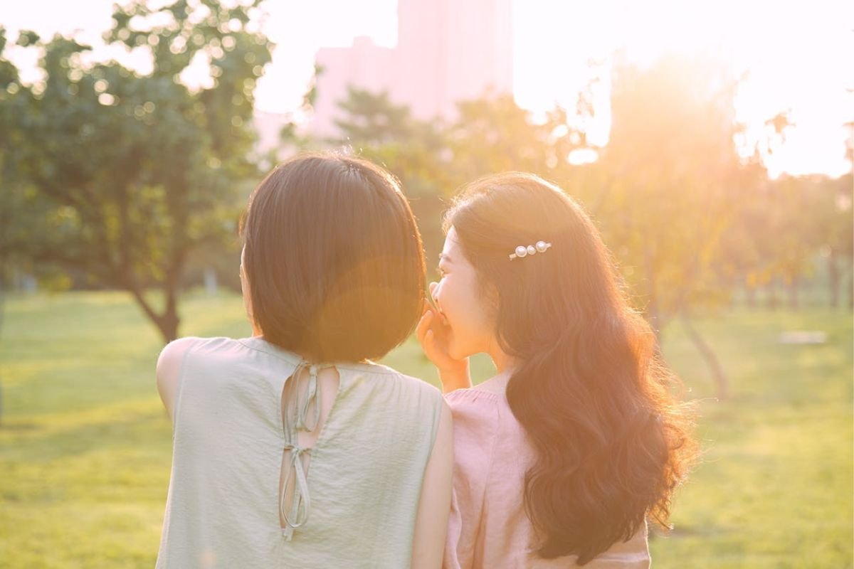 How Gossip Backfires – The Power of Spontaneous Trait Transference in Likability Woman whispering into her friend’s ear, symbolising Spontaneous Trait Transference and how gossip reflects on the speaker’s own traits.