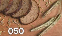 Sliced wholemeal bread with wheat stalks and grains on a rustic wooden table, symbolising natural wheat and its role in healthy eating.