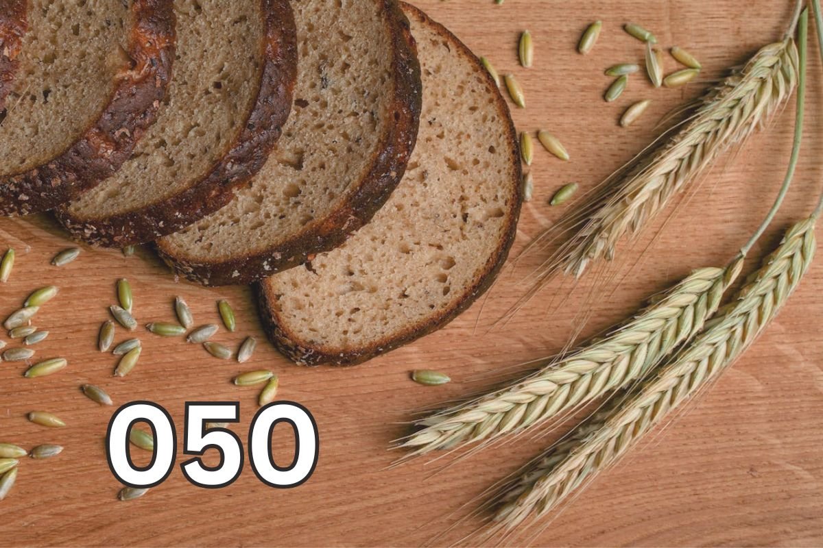 Whole Wheat Bread and Grains on Wooden Table Sliced wholemeal bread with wheat stalks and grains on a rustic wooden table, symbolising natural wheat and its role in healthy eating.