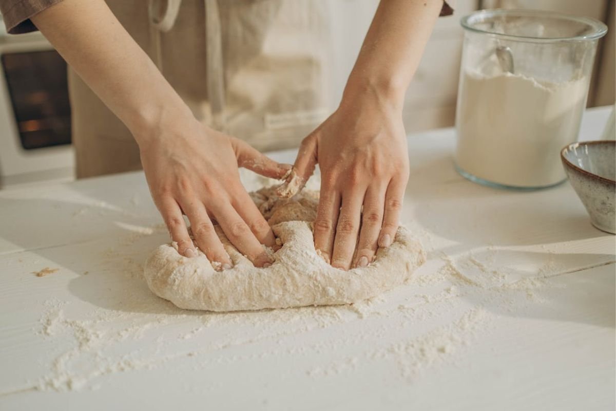 A person kneading dough on a floured table, highlighting gluten’s essential role in the texture and elasticity of wheat-based foods.