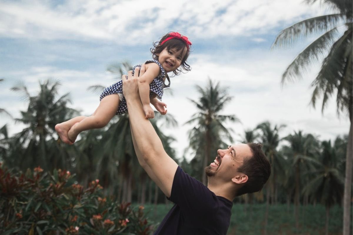 Father joyfully lifting daughter in the air, symbolising a husband’s role in building happy, secure families