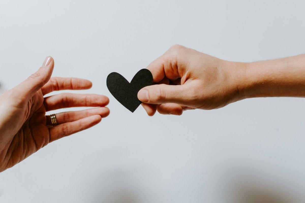 Emotional Manipulation: The Push and Pull of Love and Distance Two hands reaching for a black paper heart, symbolising emotional inconsistency and approval-seeking in relationships.