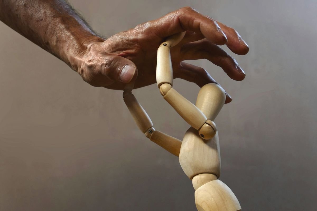 Power and Control: A Metaphor for Emotional Manipulation Close-up of a hand pushing down on a resisting wooden mannequin, representing emotional manipulation and power imbalance.