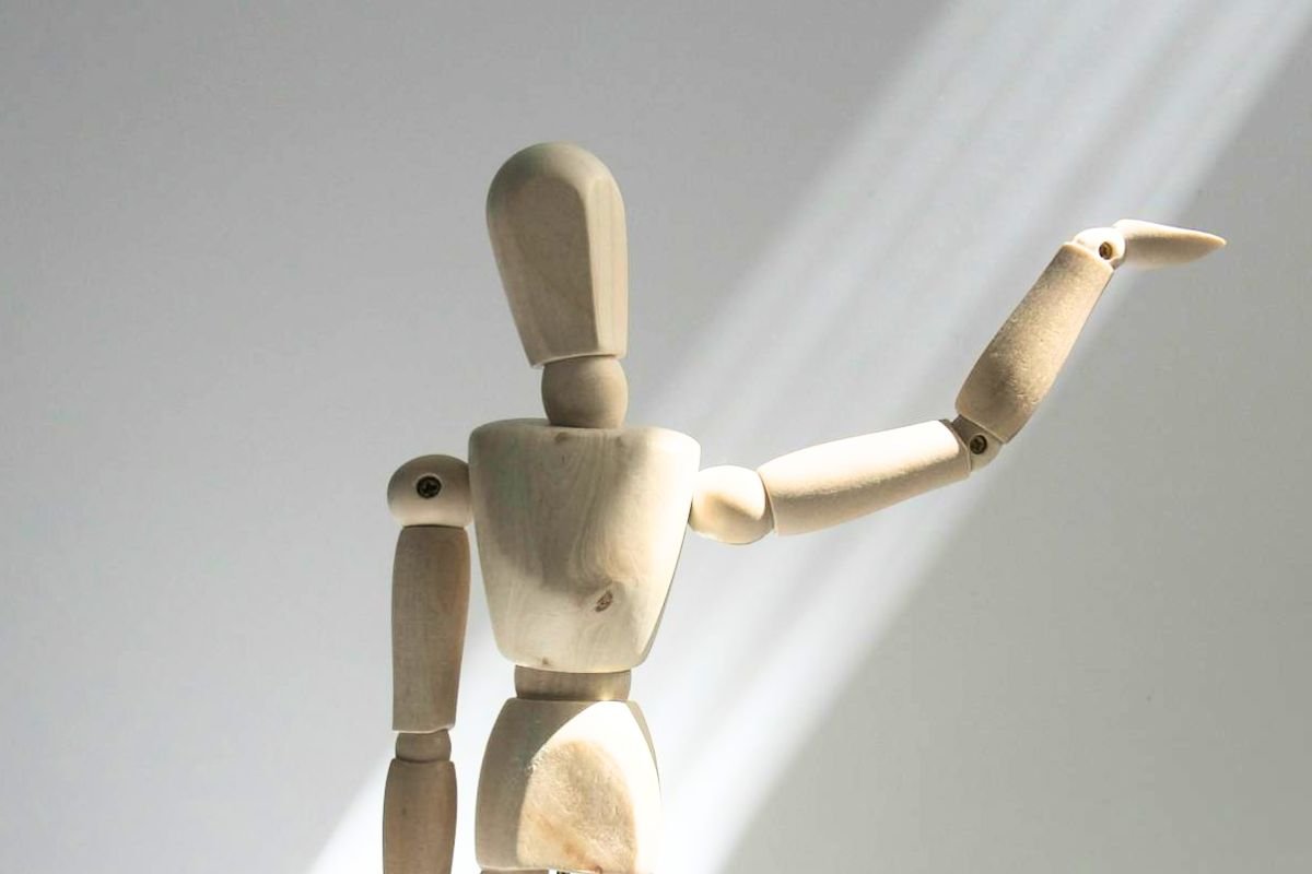 The Stagecraft of Emotional Manipulation: When Control Puts on a Show Wooden mannequin standing in a spotlight with one arm raised, symbolising the subtle performance of emotional manipulation.