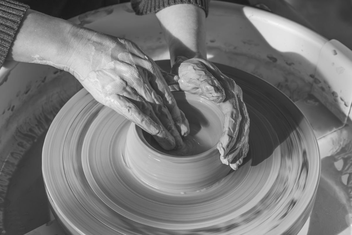 Grayscale photo of a woman sculpting a clay vase on a potter’s wheel, symbolising persistence, creativity, and everyday resilience.