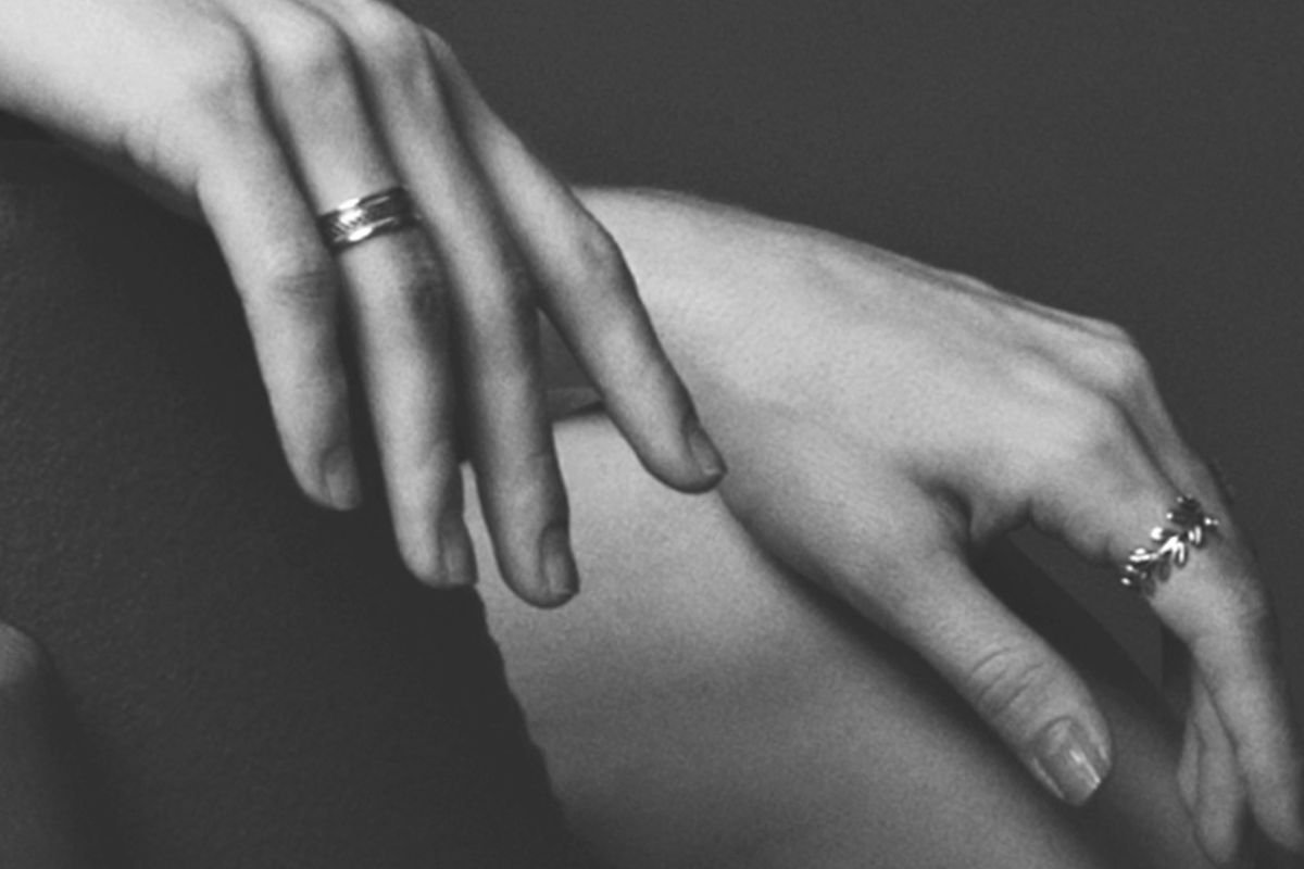 Black and white photo of a woman’s hands resting in her lap, adorned with rings, reflecting stillness and personal depth.