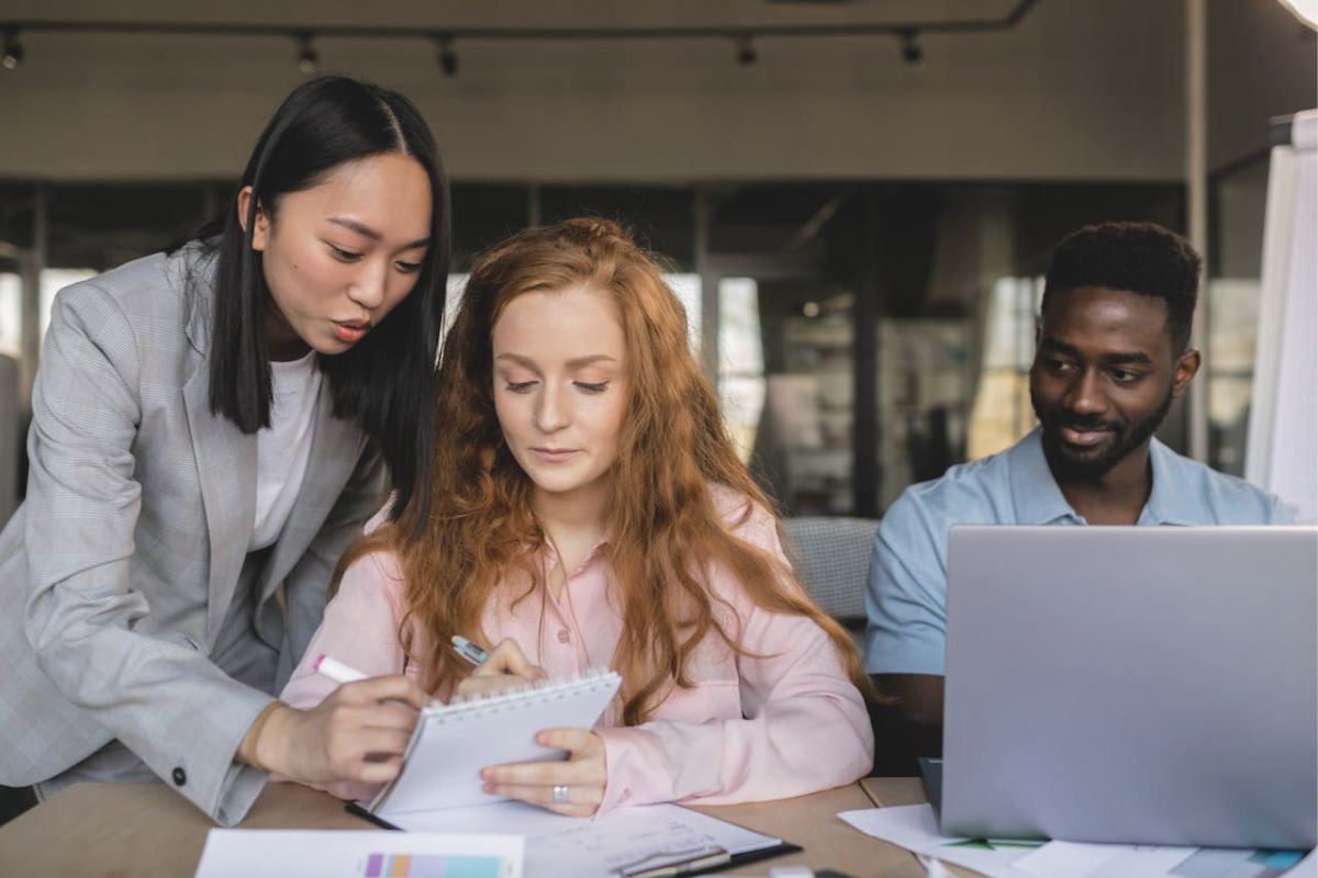 Feeling Pressured to Help? A Snapshot of People-Pleasing at Work A woman focused on work being interrupted by a colleague asking for help, representing people-pleasing and emotional obligation.