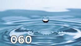 Close-up photo of a single water drop captured in motion against a blue background.