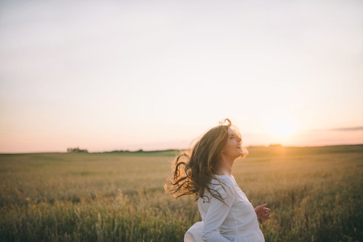 Woman smiling in a field during sunset, reflecting positivity and choosing happiness every day.