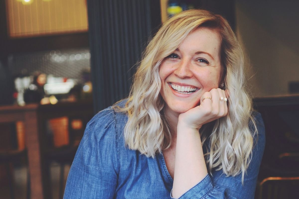 Woman seated indoors smiling warmly at the camera in a cozy room
