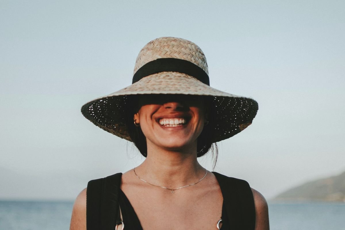 Woman in sun hat smiling brightly, symbolising positivity, confidence, and inner happiness.