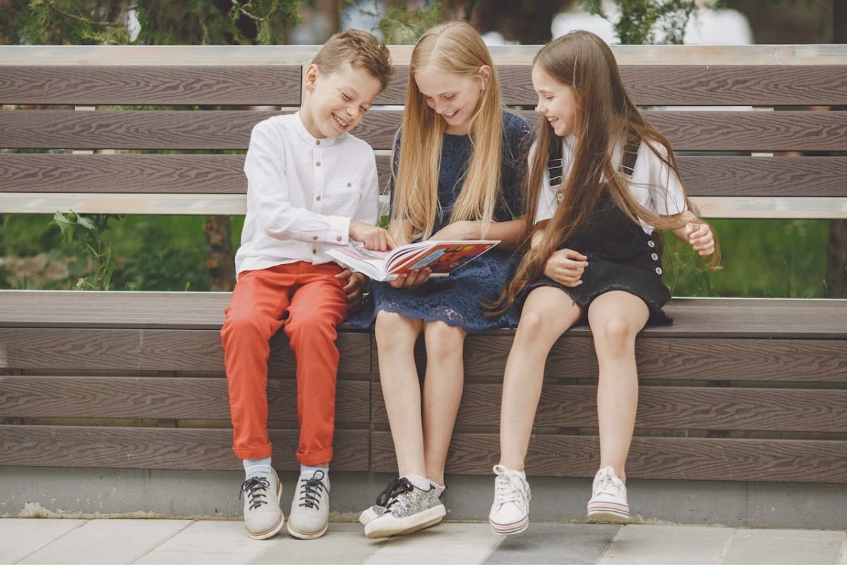 Children smiling while reading a book together, showing the simple joy and effortless happiness of childhood.