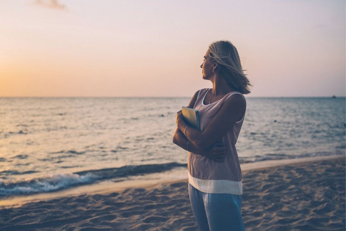 A lone woman standing on the beach during sunset, symbolising self-reliance, reflection, and peace in later life.