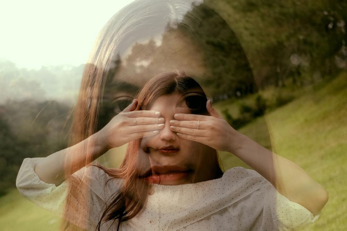 A woman covering her eyes with her hands, overlaid with an image of her weary face, symbolising emotional exhaustion and Dissociative Identity Disorder (DID).