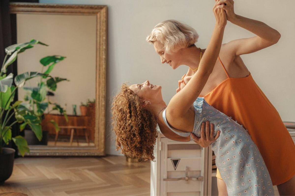 Two mature women dancing joyfully together indoors, symbolising the importance of pursuing dreams and hobbies in later life.