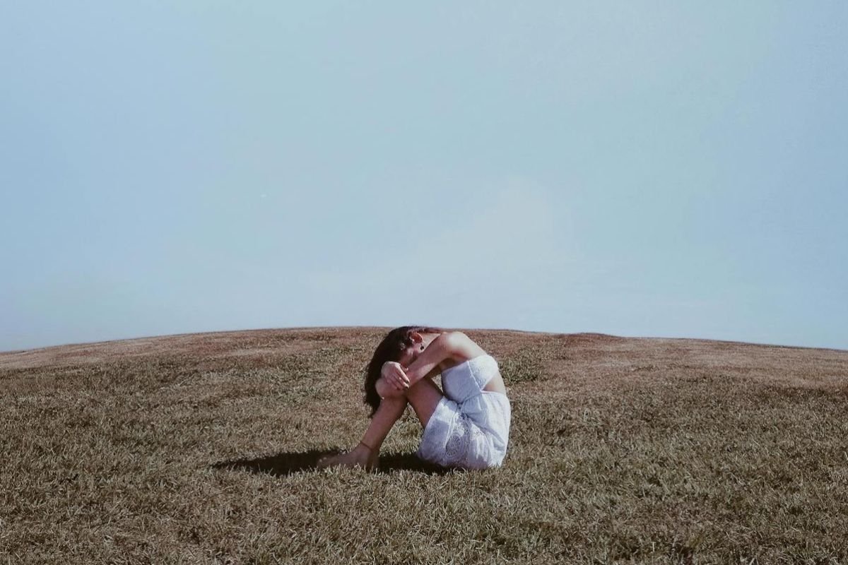 Woman sitting alone on a grassy field with her head buried in her knees, symbolising the emotional struggle of living with OCD.