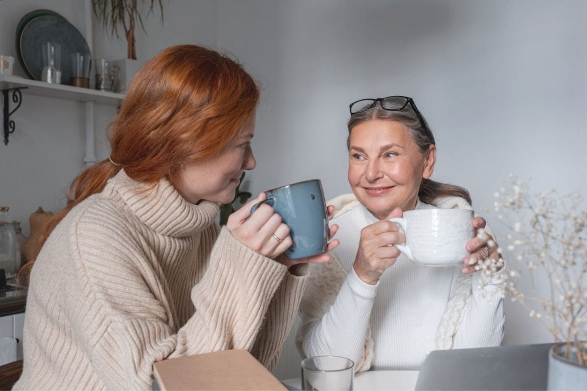 A smiling mother and daughter sharing coffee and warm conversation, symbolising trust, understanding, and peace in family relationships.