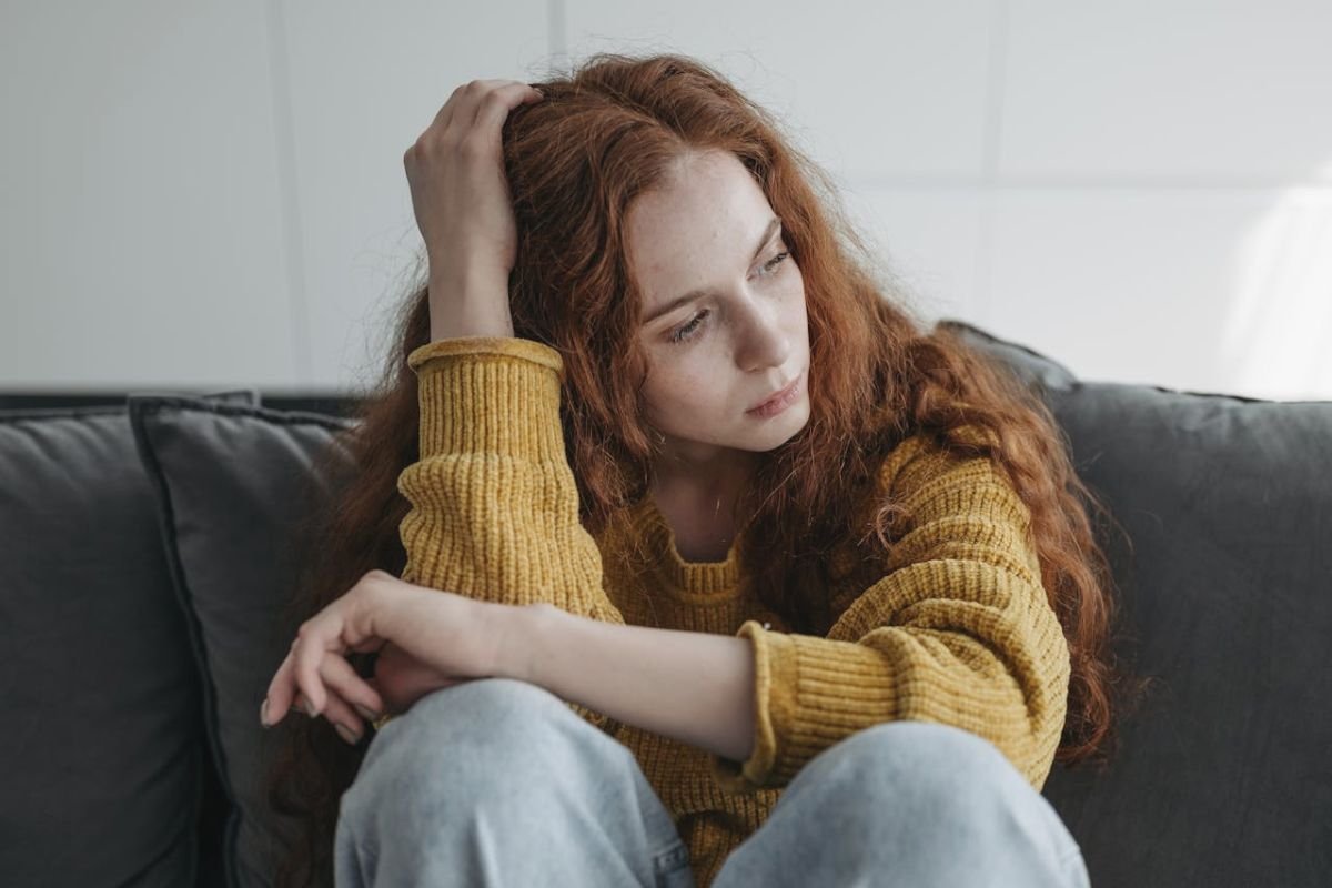 Woman sitting on couch looking upset, introspective amid heartache