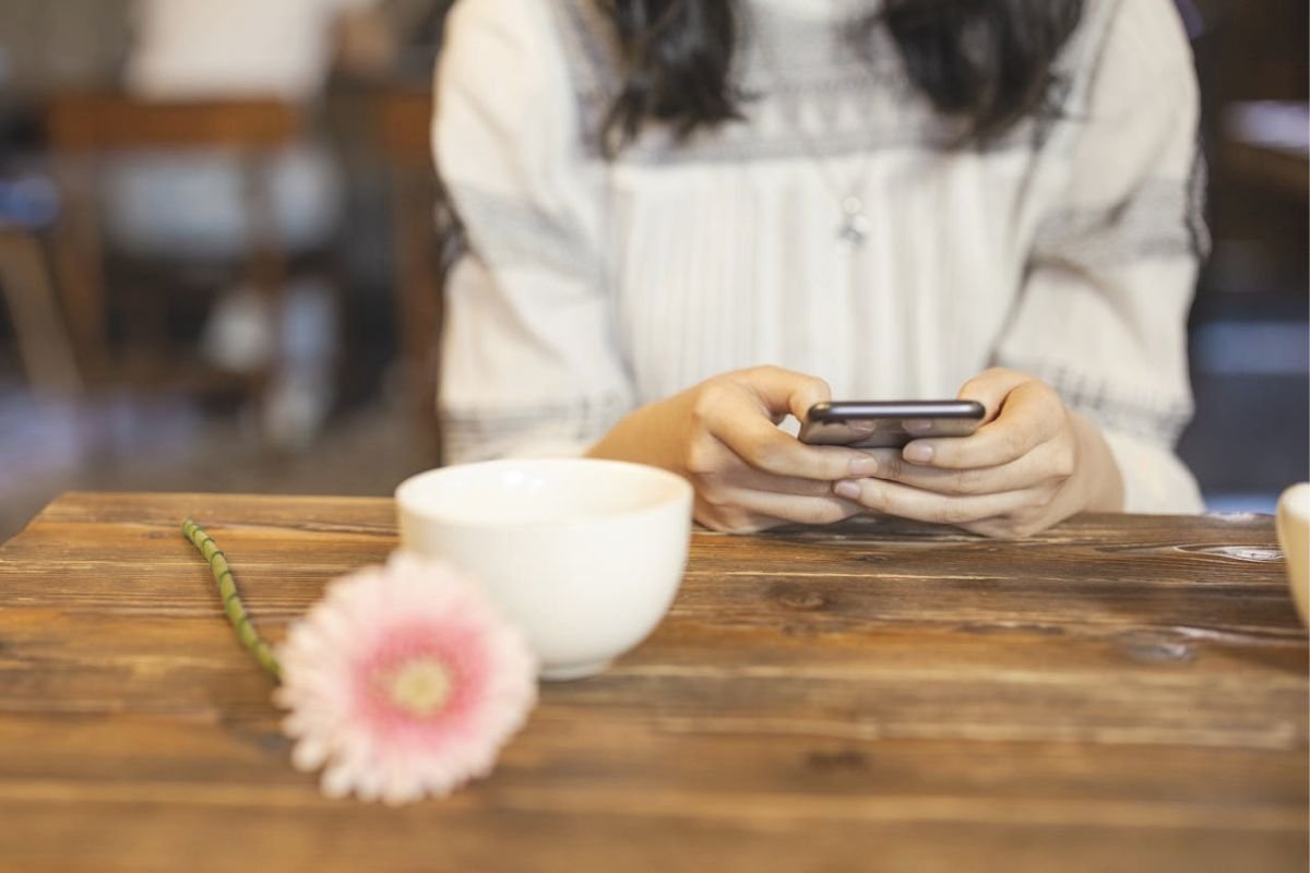 A woman using her phone beside a blooming flower, symbolising connection, support, and gradual recovery after trauma.