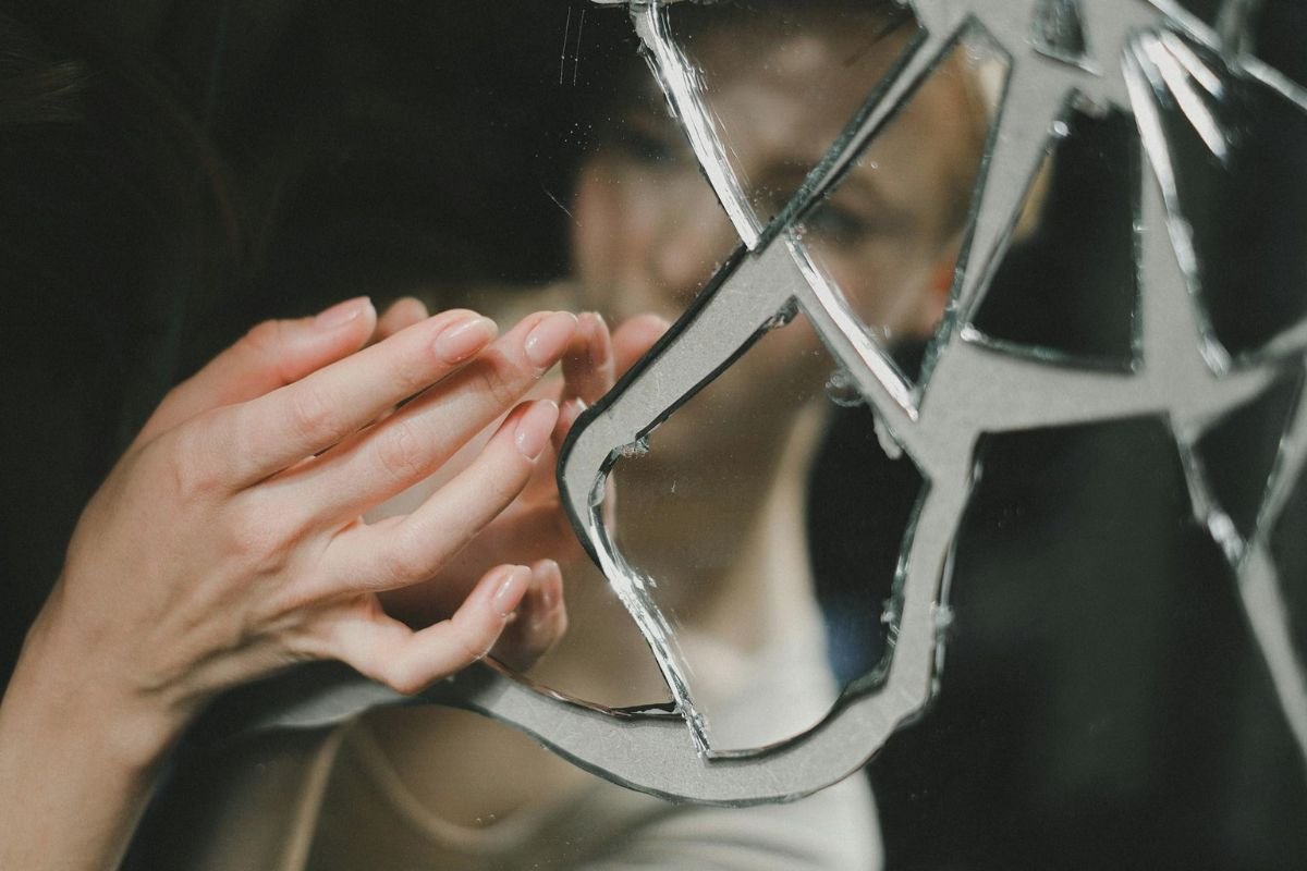 A woman gently touching a cracked mirror, symbolising how silent abuse and emotional distance can break connection in a relationship.