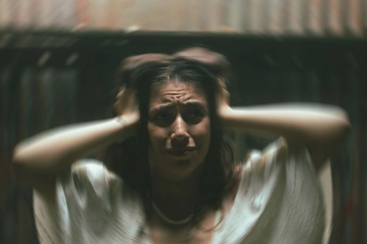 A distressed woman holding her head in her hands, illustrating intrusive memories and emotional overwhelm linked to PTSD symptoms.