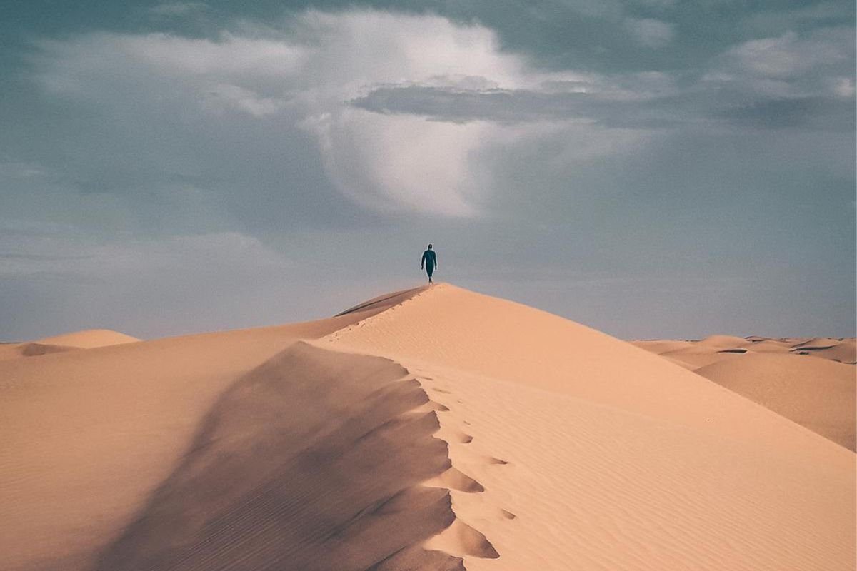 Person walking alone on a sand dune, leaving footprints behind, symbolising the personal journey of walking your own path.