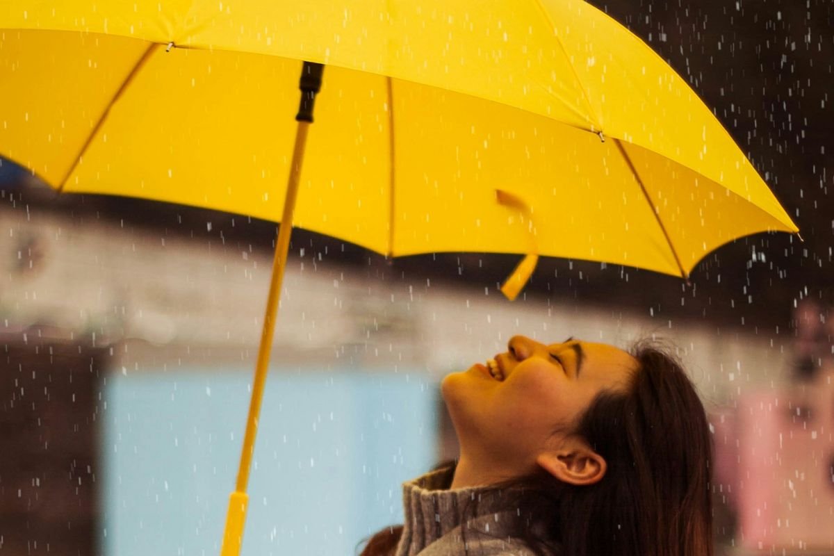 Smiling woman holding a yellow umbrella in the rain, symbolising becoming your own shelter instead of waiting for others to carry you.