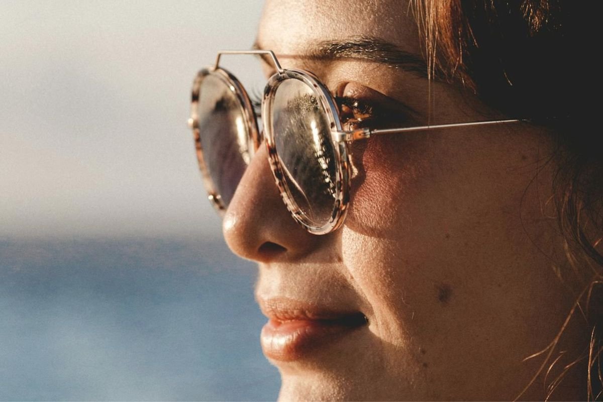 A smiling woman in sunglasses enjoying the sea alone at sunset, symbolising peaceful independence and emotional self-trust.