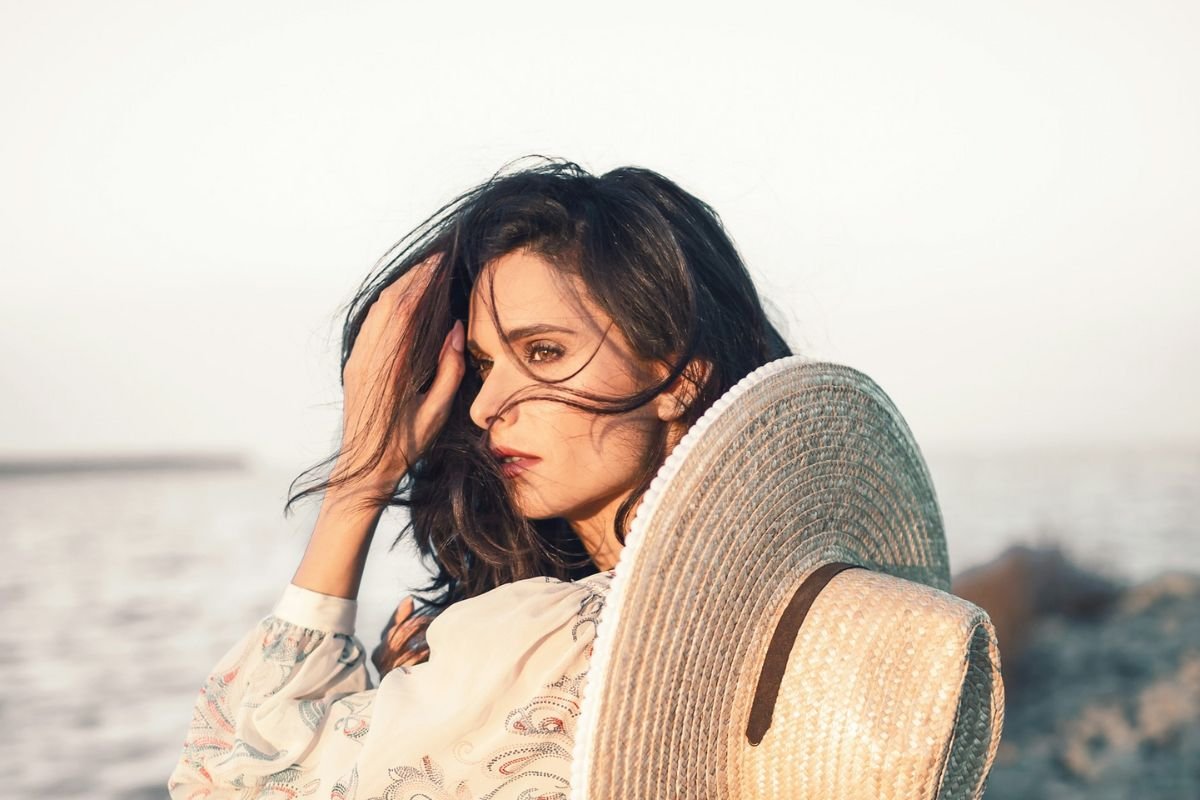 A woman wearing a brown hat gazing at the ocean, representing emotional resilience, self-trust, and confident independence.