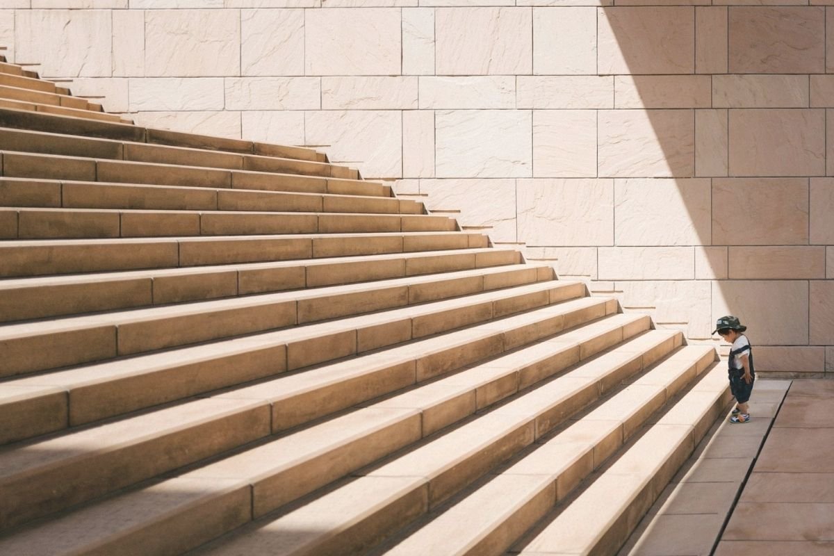Child standing before concrete stairs, symbolising the transition from education to personal growth shaped by society and lived experience.