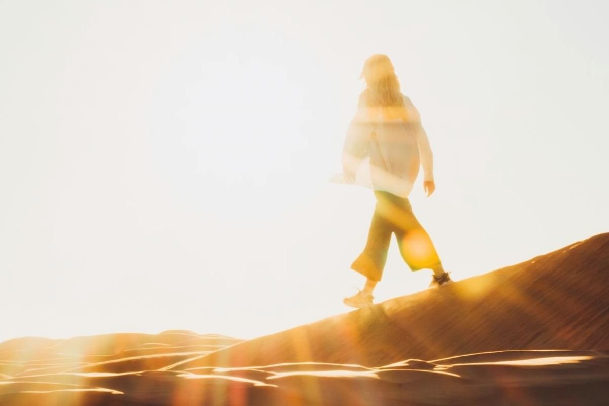 Silhouette of a woman walking toward sunlight in a desert landscape, representing self-trust, acceptance, and moving forward without needing to change others.