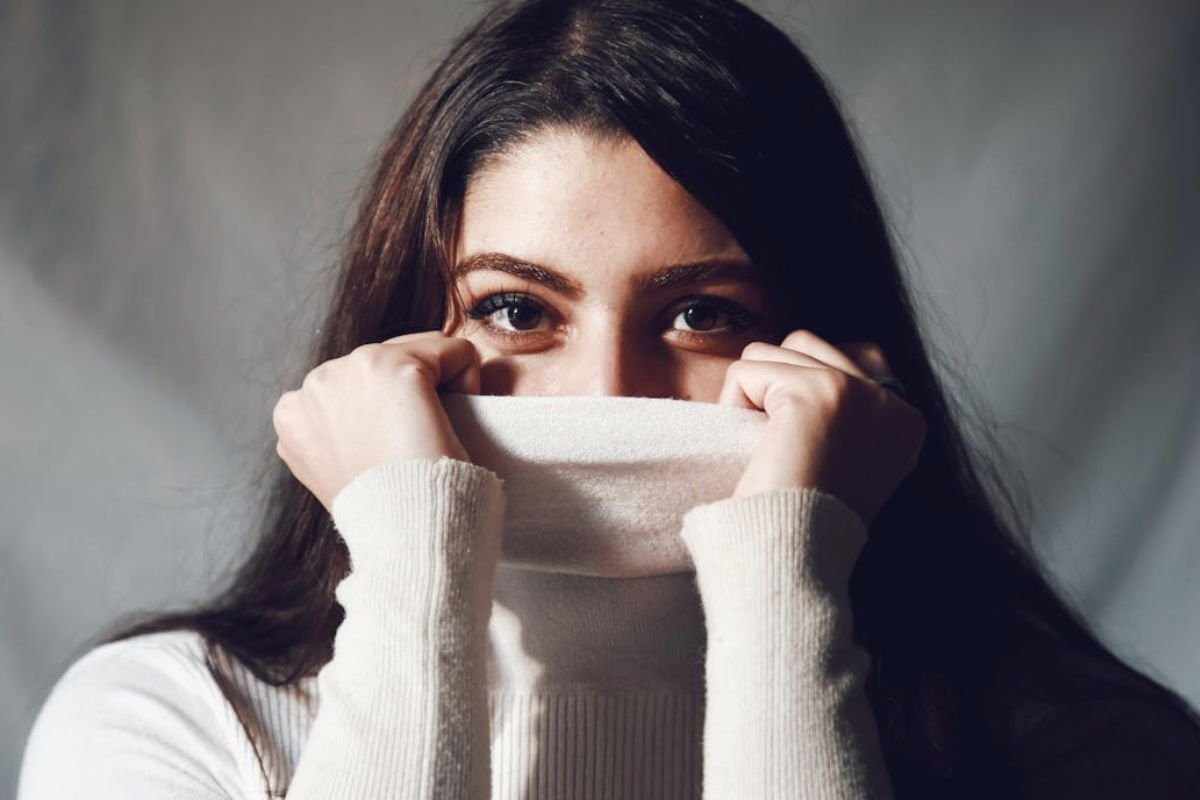 Woman partially hiding her face behind her turtleneck sweater to mask bad breath embarrassment