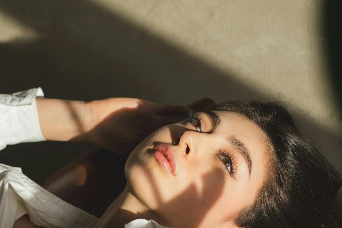 Woman lying down in sunlight looking upward representing introspection and emotional experience