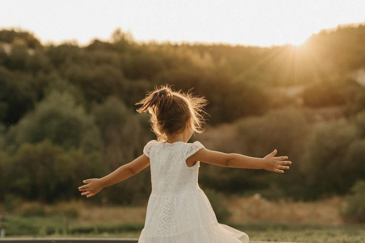 Young girl standing on grass with arms open toward sunlight, representing the importance of vitamin D in children’s bone health.