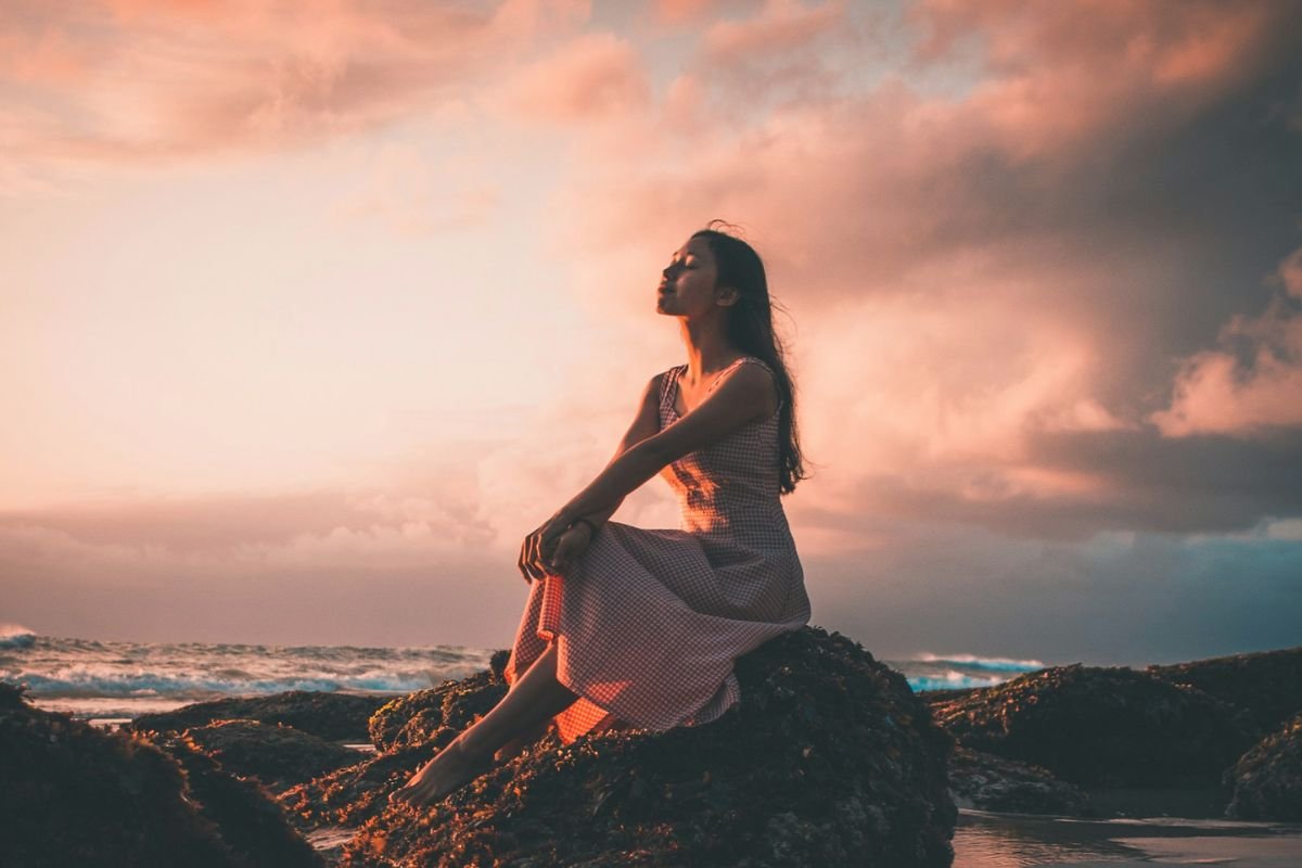 Woman sitting calmly on a rock with eyes closed, reflecting self-respect, self-love, and inner clarity in a peaceful natural setting