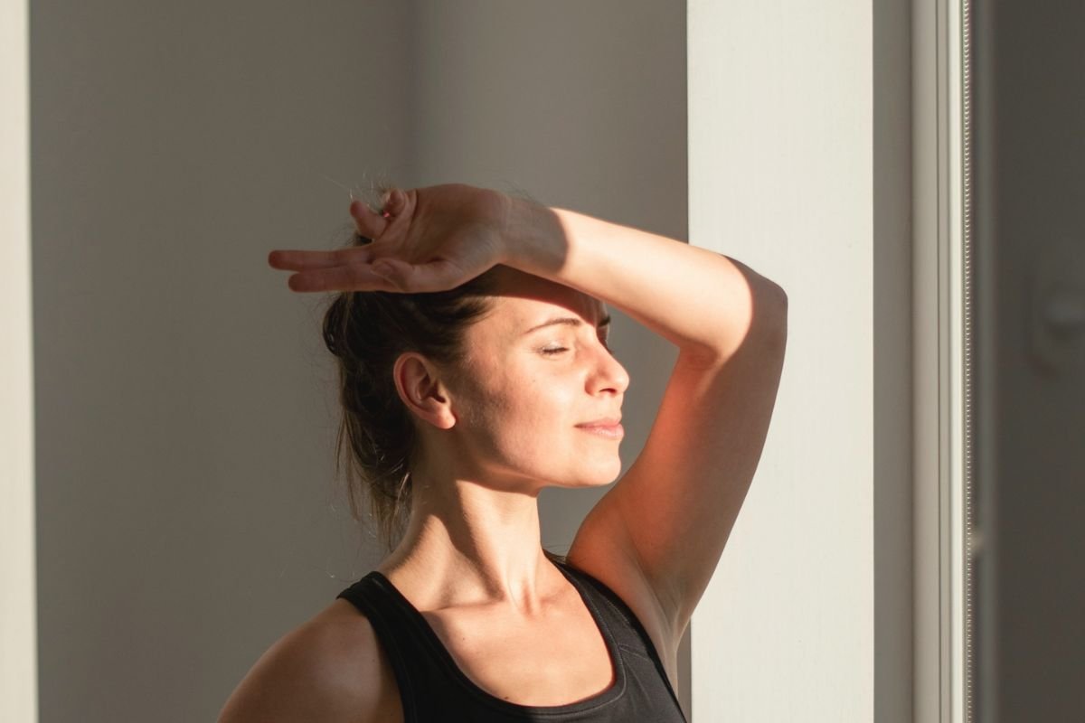 Woman standing by a sunlit window with eyes closed and smiling, symbolising vitamin D’s broader role in mood, immune health, and overall wellbeing.