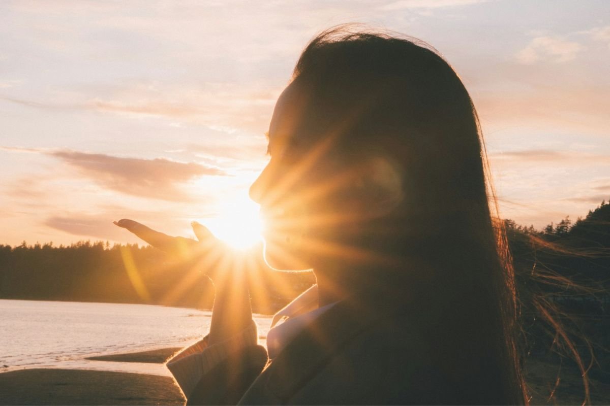 Silhouette of a woman on the beach appearing to hold the sun, symbolising safe sun exposure and natural vitamin D production.