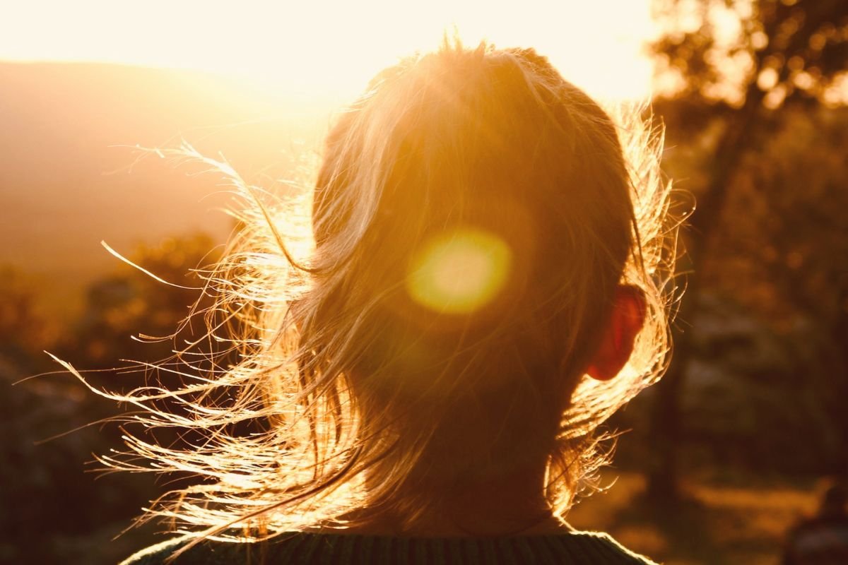 Back view of a woman with sunlight illuminating her hair at sunset, symbolising the role of sun exposure in vitamin D synthesis.