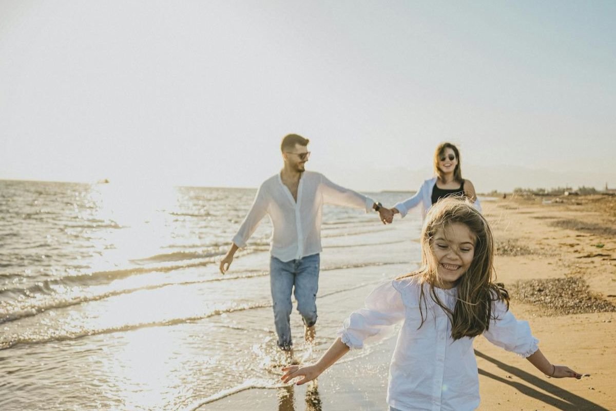 Young child running ahead on the beach while parents walk behind, symbolising independence, parental guidance, and raising teenagers with emotional support.