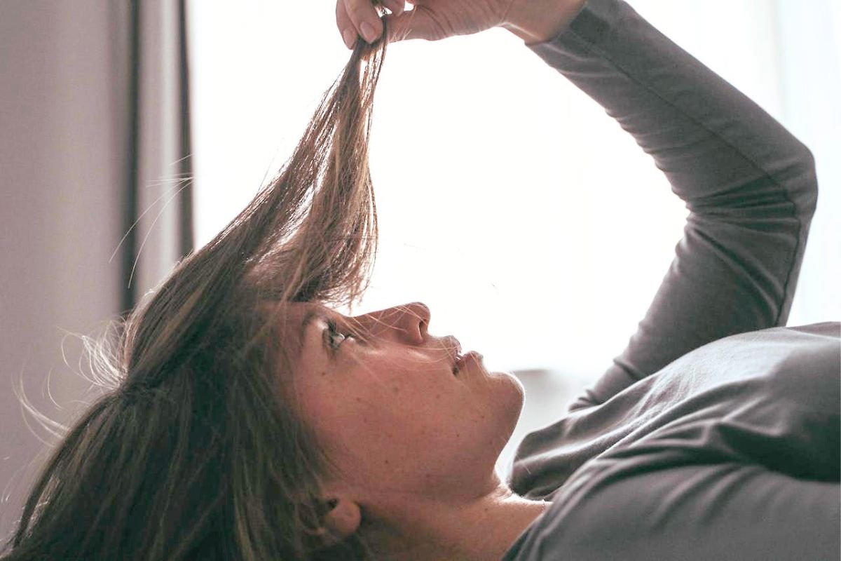 Woman inspecting thinning hair while checking scalp health and possible hair loss causes linked to stress, hormones, and nutrition.