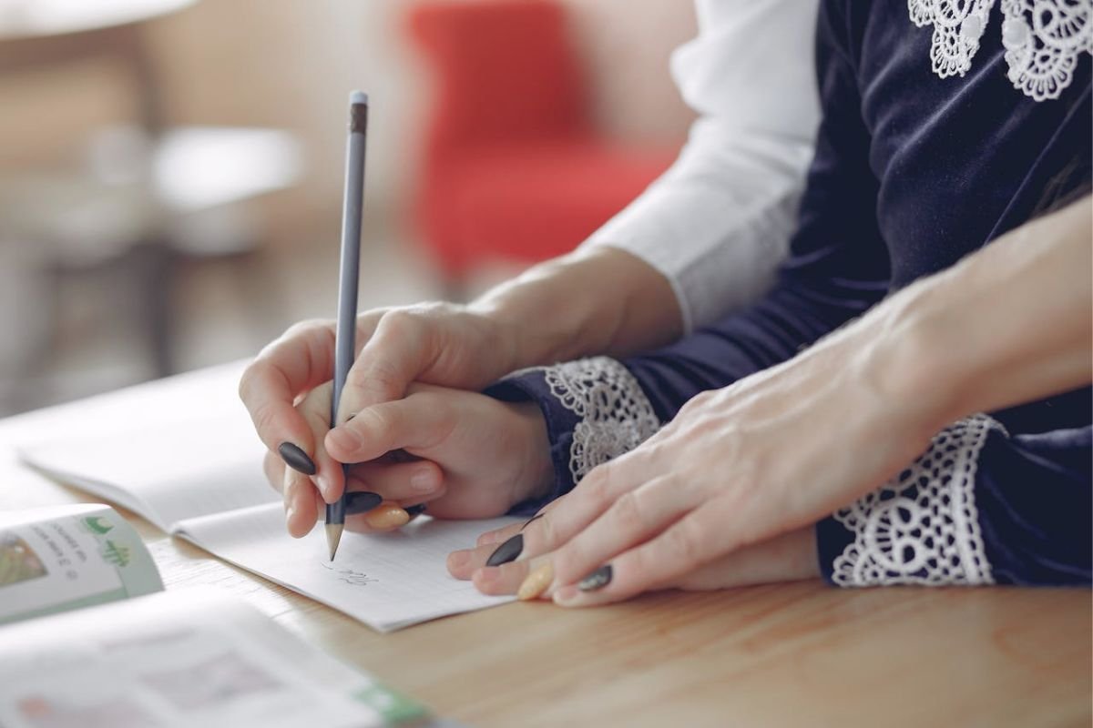 Parent holding a child’s hand while completing homework together, symbolising overprotective parenting and dependence during child development.