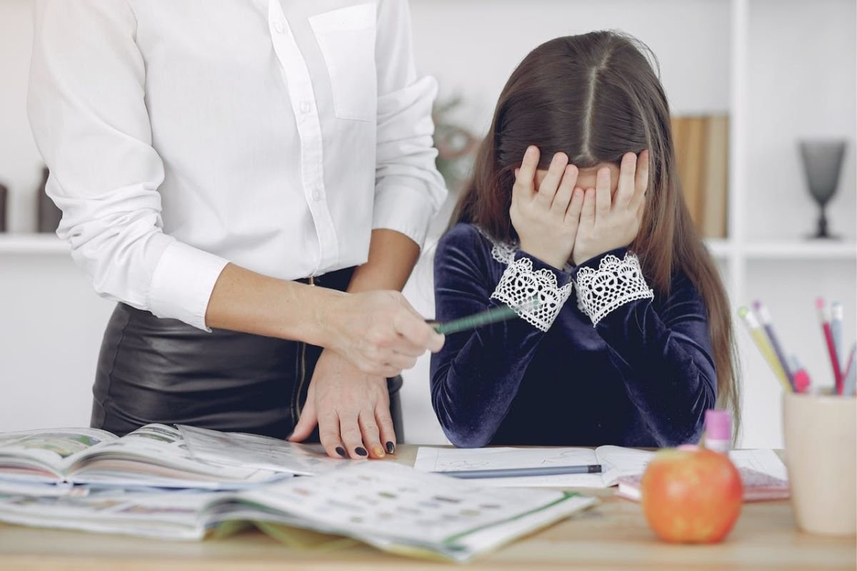 Upset child covering her face while being corrected during homework, representing strict parenting, emotional pressure, and childhood stress.