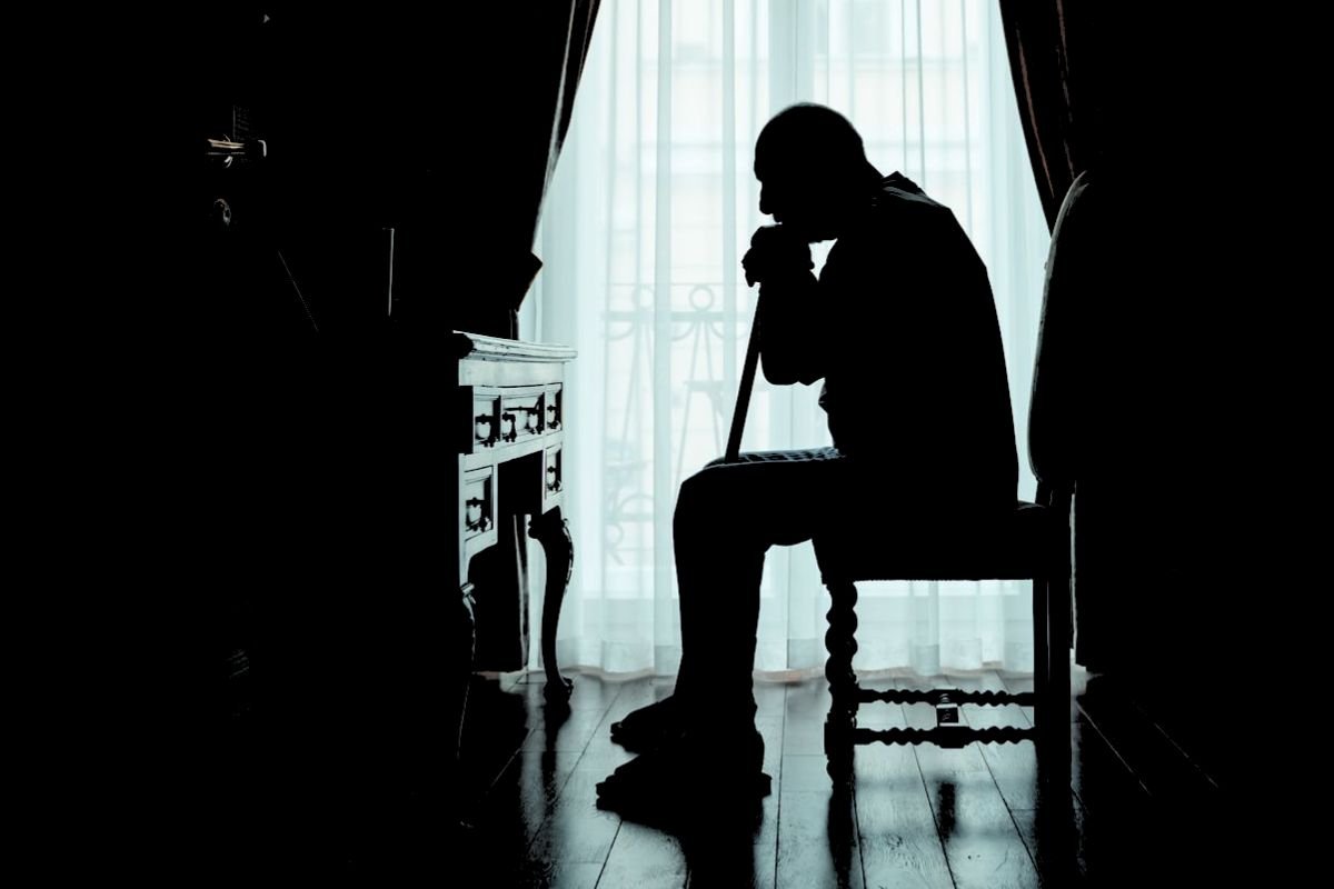 Elderly man sitting alone at home, illustrating social withdrawal and isolation that can sometimes accompany the early signs of dementia.