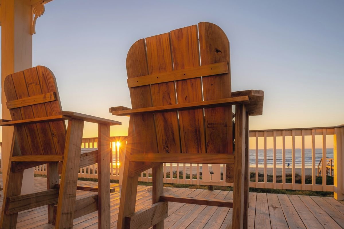 Two wooden armchairs on a porch overlooking a sunset, symbolising lifelong companionship, shared memories, and reflection in later life.