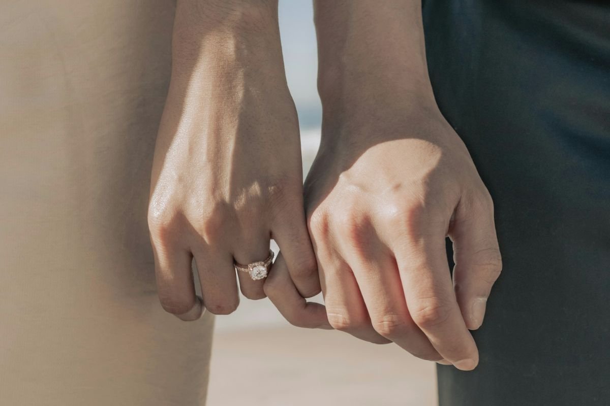 Couple holding hands on a beach, with a wedding ring visible, symbolising commitment, devotion, and lasting partnership.