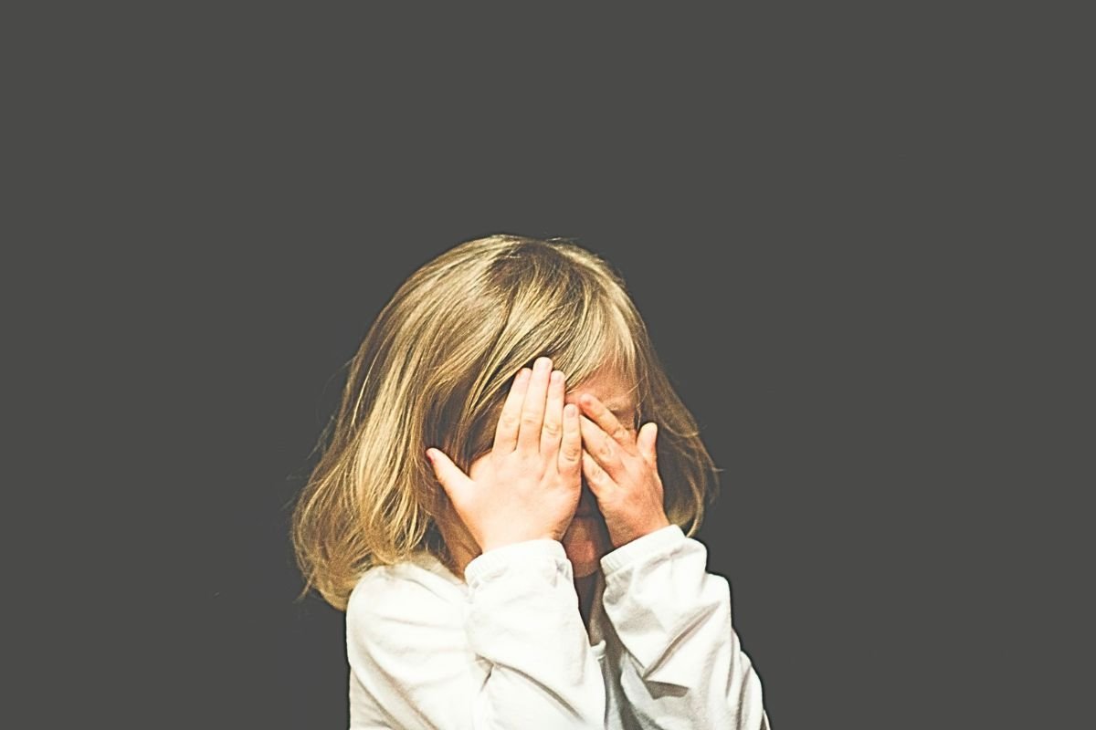 Upset child covering her face with her hands, representing childhood emotional wounds, emotional neglect, and unresolved childhood trauma.