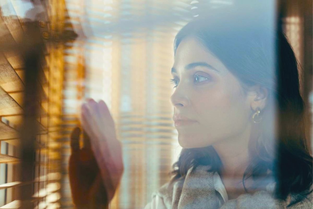Woman thoughtfully looking through window shutters, illustrating the difference between depression, major depressive disorder, and bipolar disorder.
