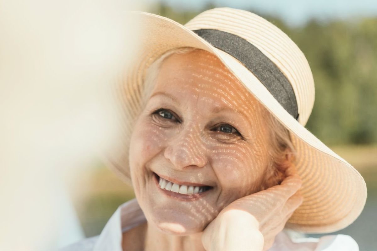 Smiling older woman wearing a straw hat by the sea, embracing solitude and enjoying life after losing a spouse.